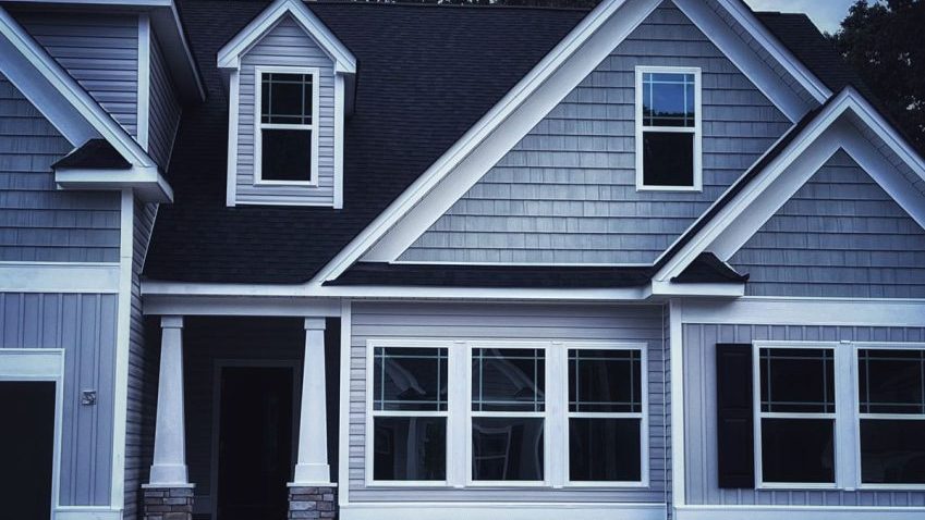 light gray house with examples of gray shakes, white accents a dark roof and horizontal siding
